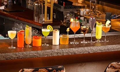 Row of colorful cocktails lined up on bar counter at UYARE